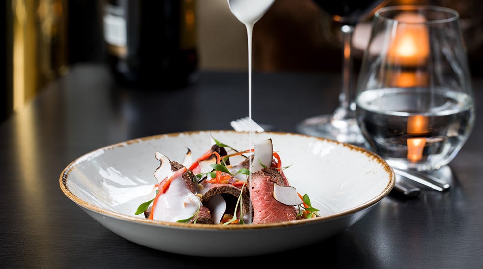 Dyp, hvit skål med kjøtt, salat, kokosflak og saus på Thief Foodbar på The Thief i Oslo 